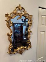 Front view showing the ornate carved gold frame and the mirror glass reflecting a room interior.
