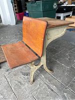 Side view showing wooden seat attached to cream-colored metal base with decorative design. Base shows discoloration and wear. Wooden seat and backrest show scratches and patina.