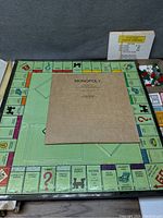 Braille Monopoly game board displayed with instruction sheet and playing pieces in box