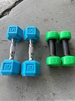 Two pairs of dumbbells showing the blue 10 lb hexagonal dumbbells with chrome handles and green 3 lb dumbbells on a concrete surface, in good clean condition.