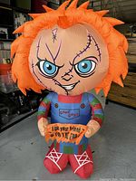 Front view of inflatable Chucky doll with detailed facial features, clothes, and sign held in hands.