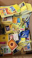 A cardboard box filled with a large bulk of mixed Pokémon cards piled up without sleeves, showing a variety of card types and colors.