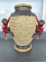 Front view of vase showing woven texture and two red monkey figurines clinging to sides as handles.