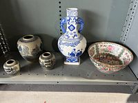 Five oriental pottery pieces on shelf including one large blue and white vase with handles, three smaller vases, and large decorative bowl.