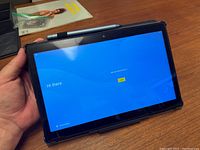 Front view of the PicassoTAB tablet powered on showing 'Hi there' welcome screen with stylus on top.