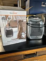 Ceramic space heater next to its original box showing product image and safety certifications.