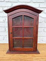 Front view of the small wooden curio cabinet showing the glass door with six segmented panels and curved top.