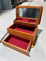 Jewelry box open showing top mirror and red velvet lined compartments, including large bottom drawer open.