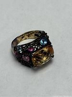 Angle showing the ring with large yellow gemstone and surrounding smaller colored gems on the dark filigree band