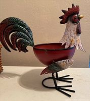 Side view of the colorful tin rooster planter, showing detailed tail feathers, comb, head and curled feet.