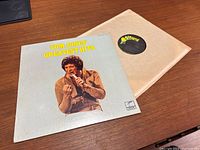 Tom Jones Greatest Hits album cover and record sleeve on wooden table.