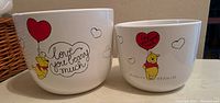 Two white ceramic bowls featuring Winnie The Pooh holding red heart-shaped balloons and the phrase "love you beary much." Larger bowl on left, smaller bowl on right.