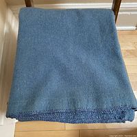 Folded blue wool blanket showing the crochet blanket stitch on edge and the wool fabric texture.