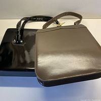 Two vintage leather purses, taupe purse in front with gold airplane closure and black patent leather purse behind