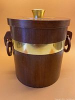 Front view of mid-century teak ice bucket showing the brass band and wooden round side handles.