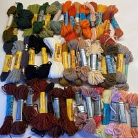 Top-down view of over 50 skeins of wool tapestry yarn arranged in multiple rows showing a variety of colors including orange, green, blue, brown, cream, and pink.