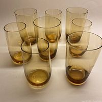 Front view of 8 amber-colored drinking glasses, showing the group with variations in height.