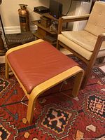 Footrest showing bentwood frame and burnt umber leather seat from side angle in living room with chair and décor.