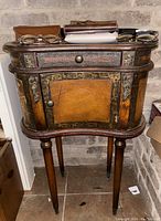 Full front view of kidney shaped accent cabinet against brick wall with glasses and cases on top.