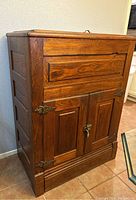 Front view of solid wood antique icebox with two paneled doors and metal hinges/latch, showing wood grain and finish.