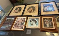 Seven framed vintage paintings on a table, including women portraits, landscapes, and floral still life.