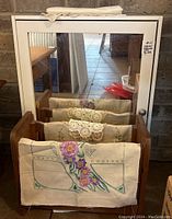 Wood laminate wall cabinet with mirrored door. Linen fabrics with floral embroidery and crochet lace on wine rack in front.