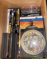 Photo showing music CDs, DVDs, Blu-ray discs and VHS tapes organized in a drawer. Titles including 'Jet Grind Radio' on a CD and 'Logan' on a Blu-ray/DVD case are seen.