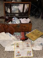 Vintage small hand tooled genuine leather trunk made in Mexico by Flores with assorted vintage ladies handkerchiefs spread around it.