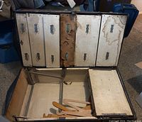 Open antique trunk showing interior wood drawers with metal handles and keyholes, worn and damaged surfaces.