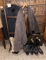 Full view of vintage wooden valet stand holding a charcoal pinstripe men’s suit jacket and a light brown suede leather jacket with paisley lining. Below are four pairs of leather boots in black, light tan, brown, and white, all size 7, and a vintage greenish Samsonite briefcase.