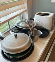 Multiple pots and pans stacked with lids and mini kitchen tools included, placed on a windowsill.