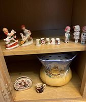 Porcelain figurines of children in various poses, 4 decorative thimbles, small dish, and miniature creamer cup shown on wooden shelf