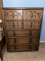 Front view of vintage mid century modern wood chest with five drawers, showing decorative grid and arch panel details on upper drawers and solid panels below.