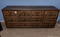 Front view of vintage Mid-Century Modern wood dresser with nine drawers, decorative carved fronts, and black metal handles.