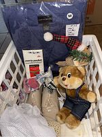 Lot items displayed in a white basket including pajamas in packaging, tan patent leather shoes, handkerchiefs, crochet cap, plush toy, and ornament.