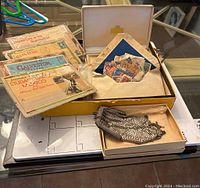 Vintage postage stamps in a box alongside postcards and silver metal mesh handbag arranged on a table.
