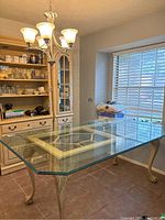 Front and top angle view of the dining table showing rectangular beveled tempered glass top and ornately carved wood base with cabriole legs and claw feet against a neutral room background.