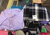 Purple top and black and purple plaid coat folded on table