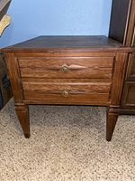 Front view of the mid-century modern wooden end table showing two drawers with brass flower shaped handles and tapered legs.