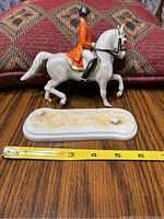 Side view of the rider on the white horse separated from its base, showing measuring tape approximately 6 inches long.