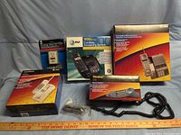 Four AT&T phones in boxes with accessories including cords and manuals, set on a black background with ruler.