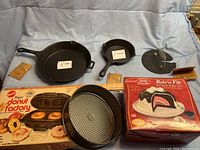 Photo of the full lot showing all items including two cast iron skillets, grill press, donut maker pan, and boxed Bake'n Fill set.
