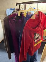 Red fleece Mickey Mouse jacket, grey jacket, purple and blue snow pants hanging on rack