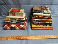 Two stacks of assorted cookbooks showing variety in size, color, and topics, laid on a blue cloth background with a Home Depot ruler for scale.