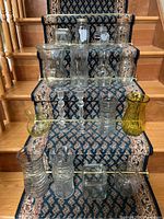 Glassware items arranged on carpeted stairs including vases, Mason jars, candlesticks, and colored glass vase.