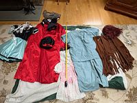 Photo of the full costume lot spread on floor, showing all pieces including geisha costume with wig, waitress dress, hippie vest and wig, ballerina dress, and scrubs