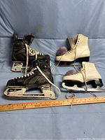Two pairs of ice skates - black hockey skates size 7 and white ladies figure skates size 6 with purple pom-poms. Both pairs are worn and sized.