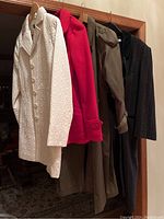 Four women's winter coats hanging on a rack including white quilted, bright red, brown, and dark pinstripe coats