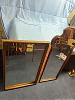 Two rectangular wall mirrors with wooden frames resting against a blue cloth backdrop. Floor setting visible with other furniture.
