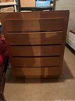 Full front view of the 5-drawer dresser showing the flat drawer fronts with integrated pull grooves in medium brown wood finish.